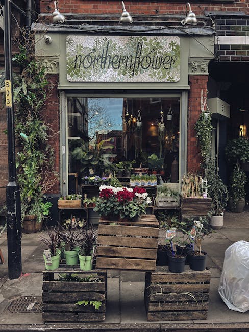The storefront of Northernflower, a floral shop with a vintage-style signboard, situated on a brick building exterior. Outside, there are wooden planters filled with potted plants and flowers, includi